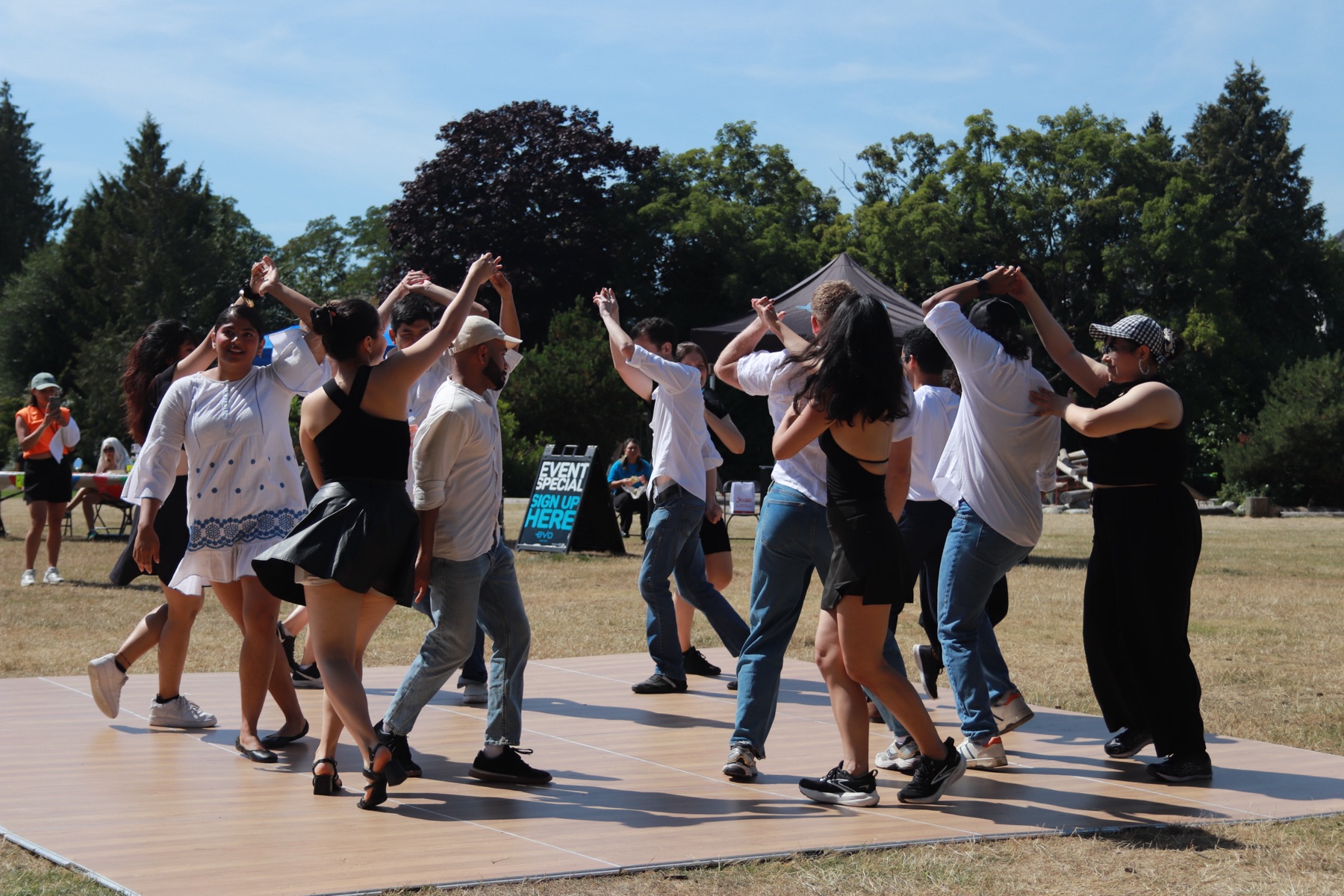A rueda circle of dancers with arms raised on the dance floor in the summer sun at VOSF 2025