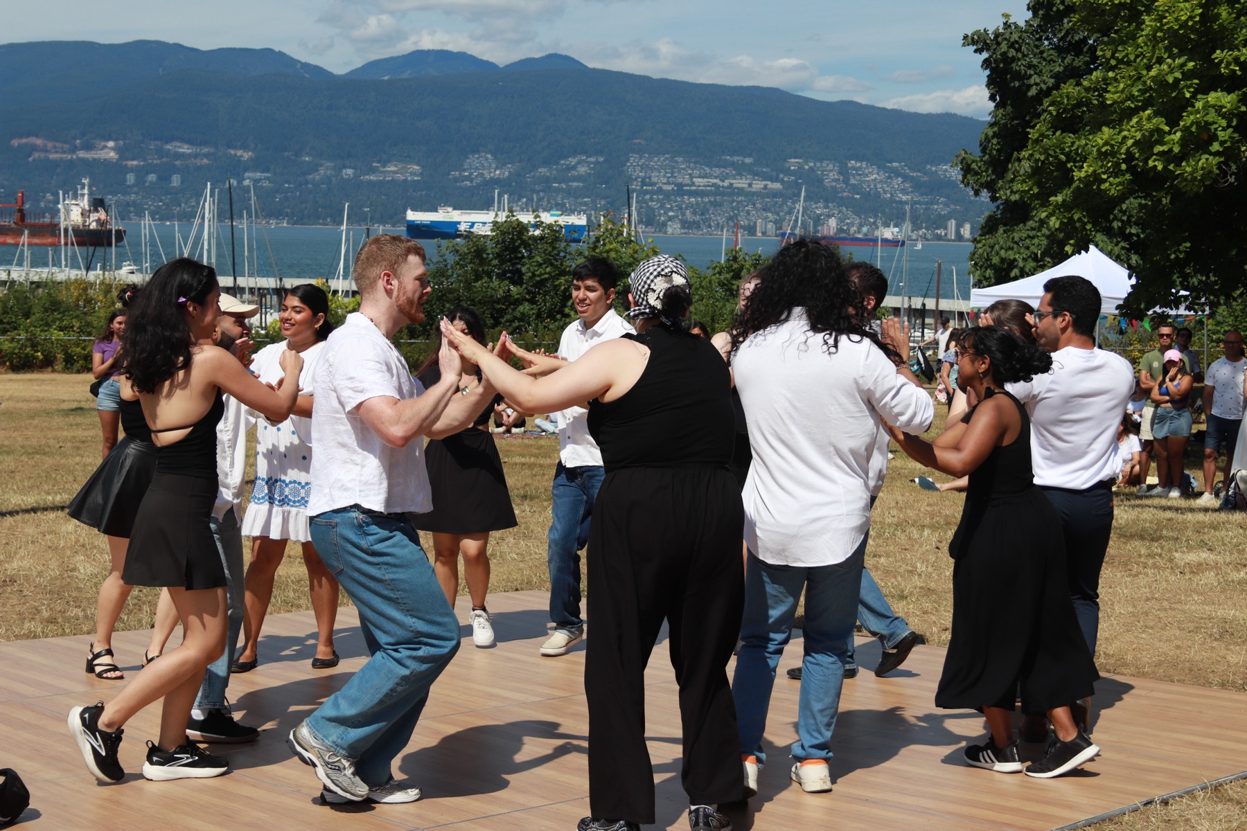 Dancers social dancing on the outdoor floor at VOSF 2025, with English Bay, sailboats, and the North Shore mountains behind them